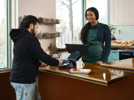 A customer paying a smiling barista at a café counter