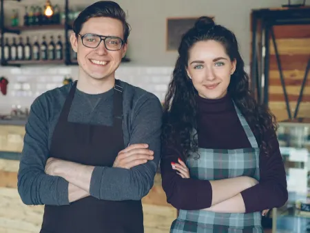 Two smiling café owners standing in front of their counter