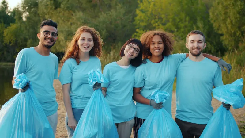Smiling volunteers in matching shirts holding bags of litter they collected in a park