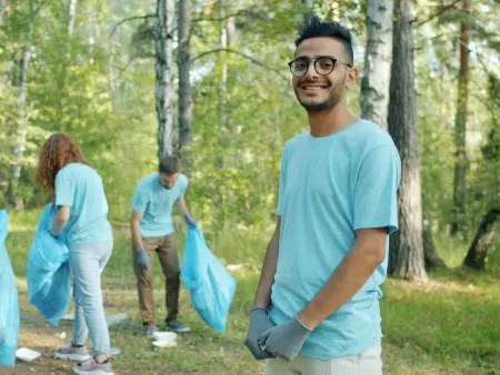 A volunteer smiling during a park cleanup, others collecting litter behind him